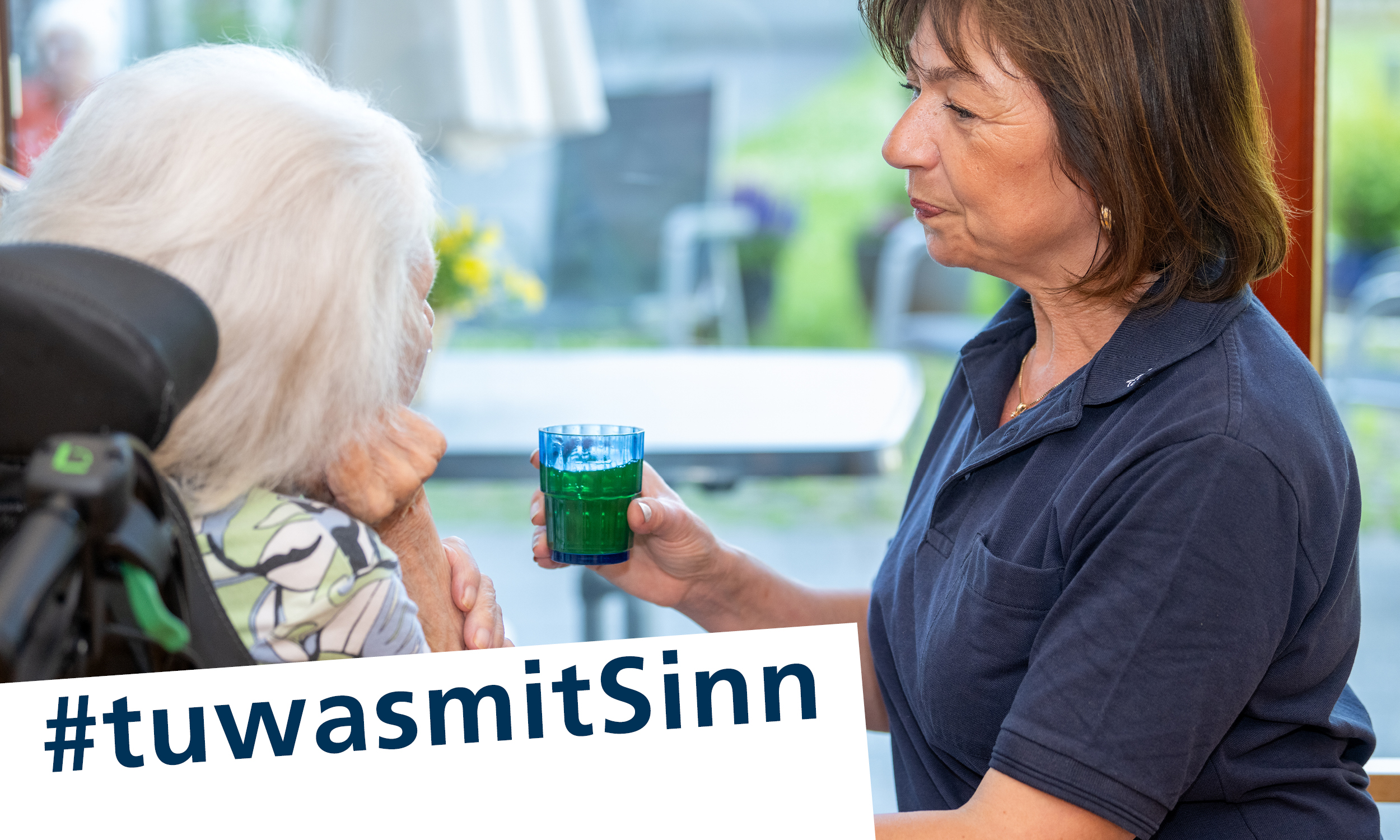 Eine Pflegekraft gibt einer Bewohnerin ein Glas Saft - darunter der Slogan: tu was mit Sinn